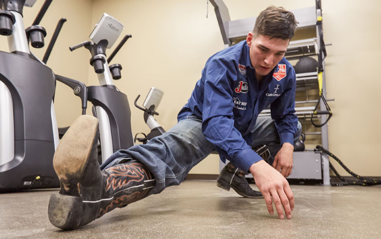 Jess Pope stretches before rodeo wearing western clothes and cowboy boots.